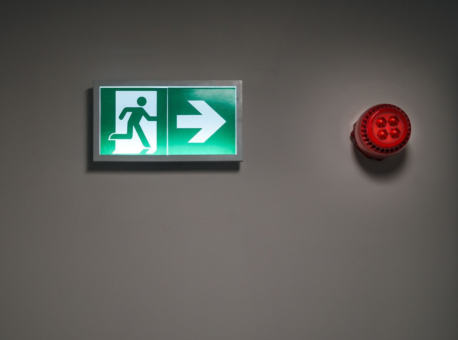 A red alarm bell beside a green emergency exit sign
