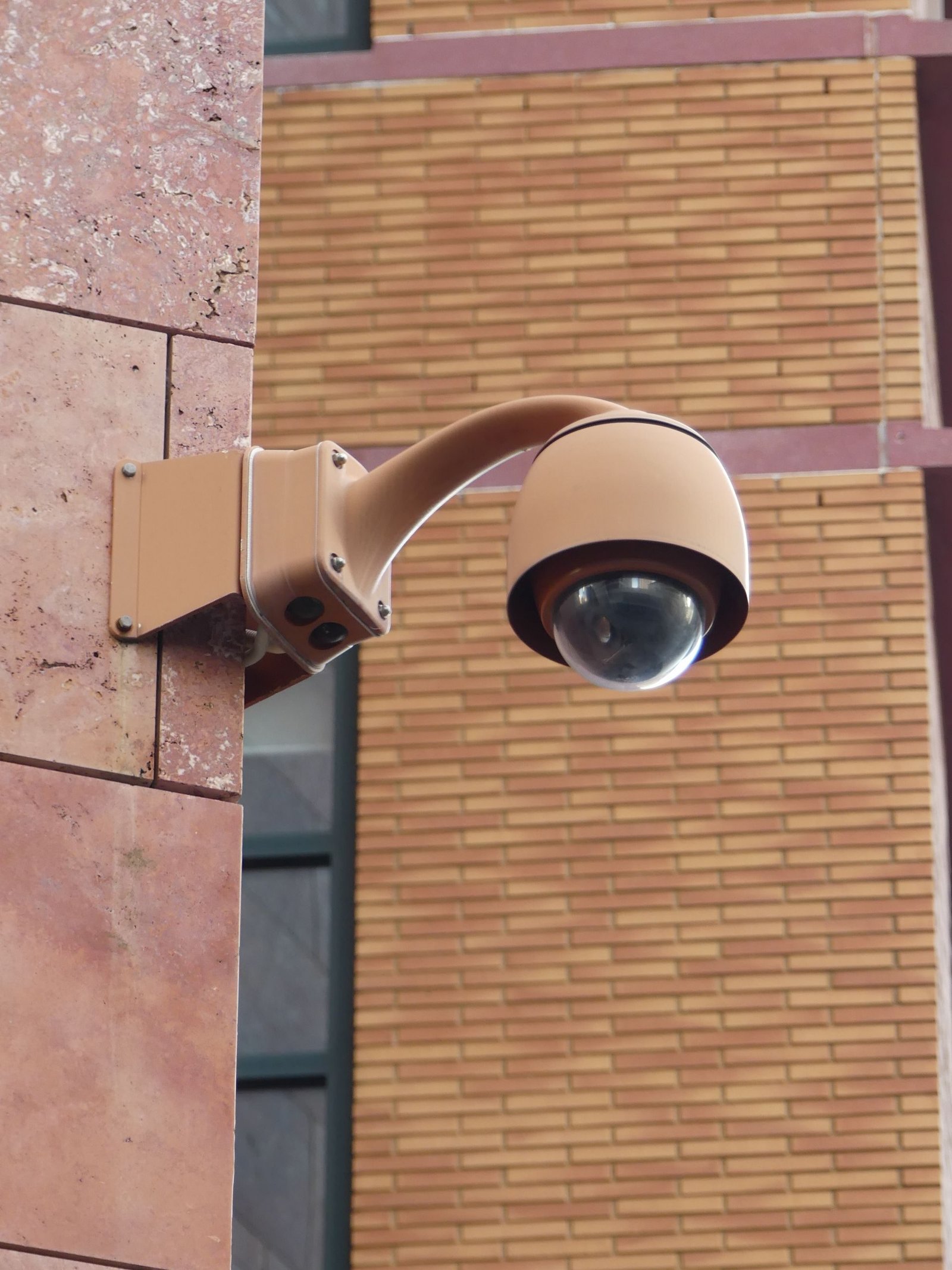 A PTZ dome camera on a bracket against a brick wall