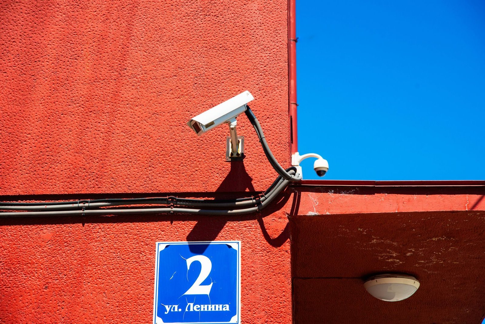 Two CCTV cameras mounted on a red building wall under a blue sky